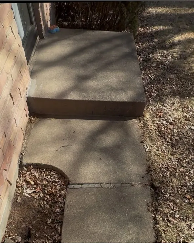 Dark, stained concrete step beside a brick wall before pressure washing
